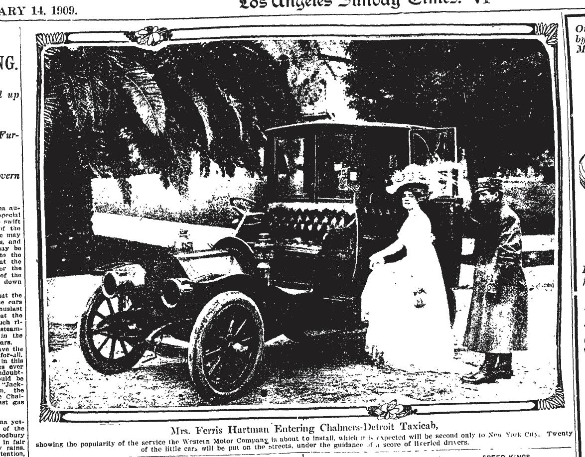 February 14, 1909: A woman in a long dress gets into an old-fashioned horseless carriage taxicab as a man holds the door for her. 