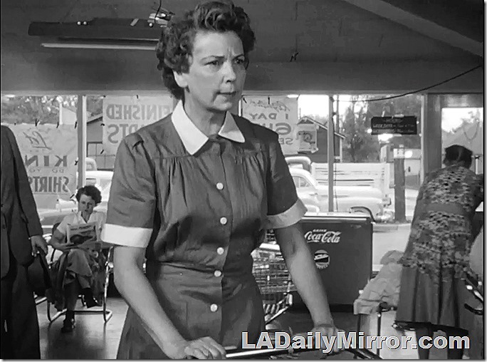 Dec. 13, 2021, Mystery Photo, a woman in uniform at a laundromat. Customers wait in the background and there's an old-fashioned Coke machine near the window
