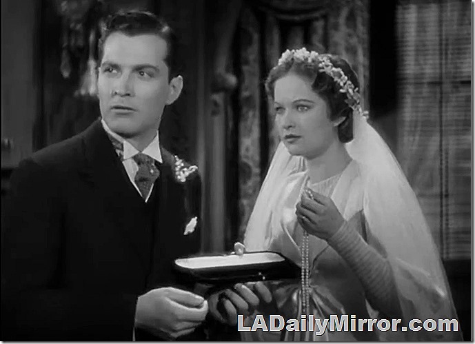 Groom and bride in 1910 setting. The bride has a long veil and is holding a string of pearls