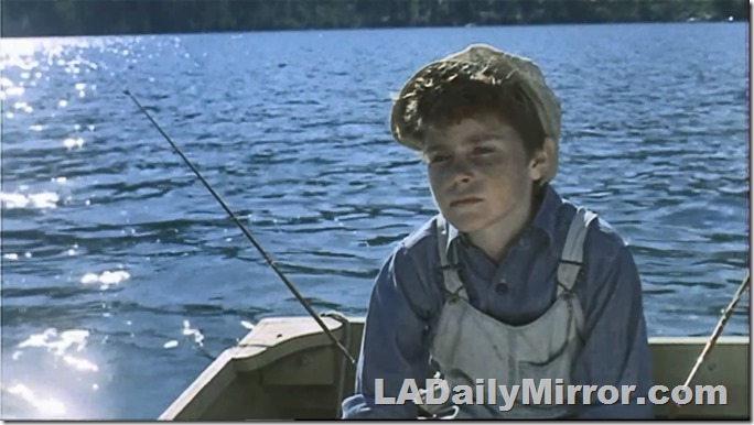 Boy in overalls and a newsboy cap fishing in a boat