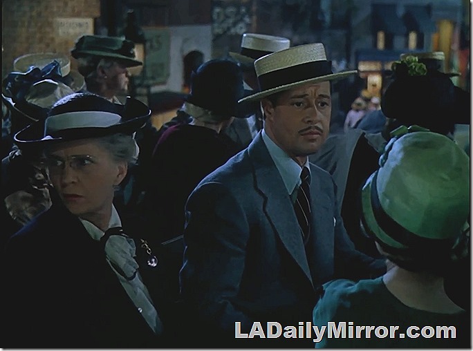 A crowd of sightseers, a man in a suit and boater hat