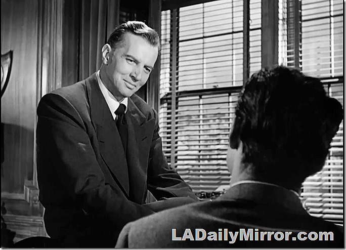 Man in suit sitting on desk. The man is sitting on the desk, the suit isn't. Well, it sort of is, but only because the man is wearing it. The suit, not the desk. 