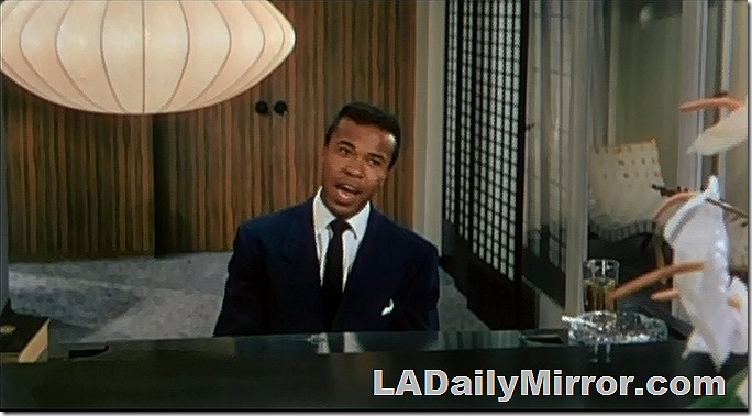 Man in a coat and tie is sitting at the piano and singing