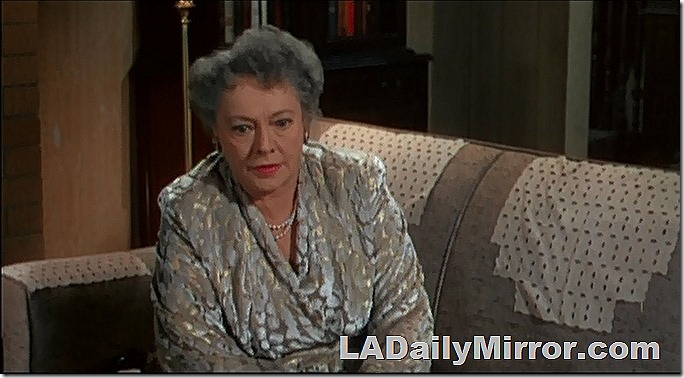 Woman sitting on a couch. She is well dressed, wearing earrings and a necklace