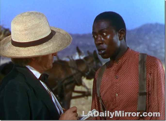 Mystery fellow in a red dotted shirt and suspenders talks to man in big, floppy hat