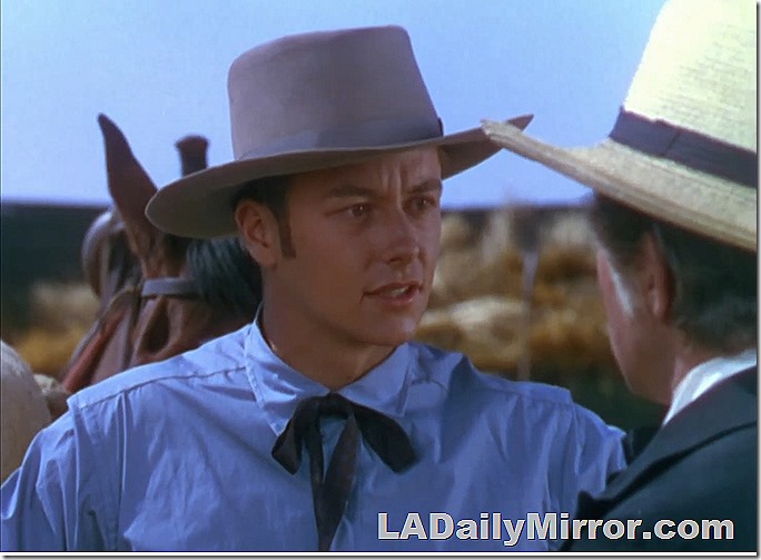 Young man in a shirt with a string tie and hat. A horse is in the background. 