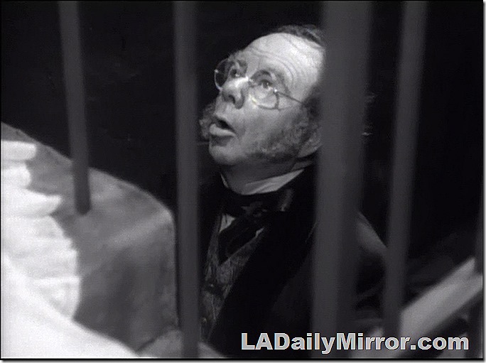 Man with glasses and long sideburns looks through metal bars