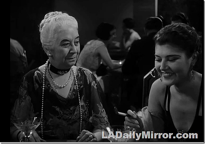 Older woman, modestly dressed, with long strings of pearls. A younger woman, very short hair, smoking a cigarette, in an elegant dress with bare shoulders and a plunging neckline.