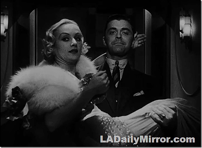 Our leading man is carrying our elegantly dressed leading lady. She may be concerned about whether he's going to trip over a cable. 