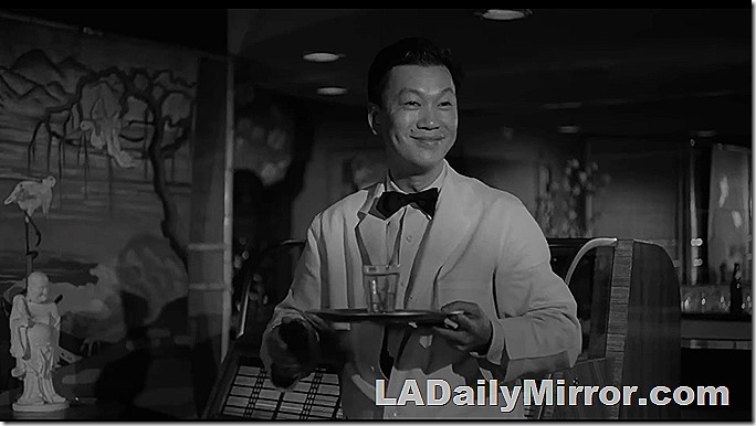 A waiter in a white coat. He is carrying a glass on a tray