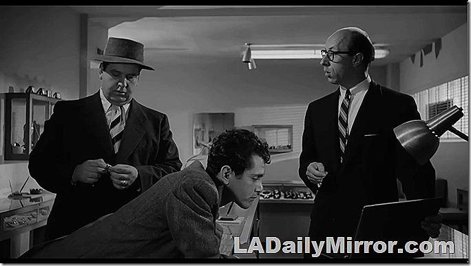 A bald man wearing glasses talks to two disreputable looking gents. 