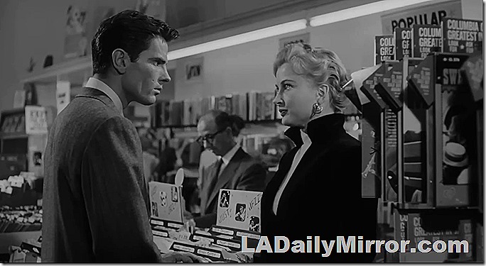 Man (in suit) and woman (short blond hair) in record store. 