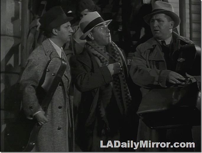 Three men in hats and long coats. The center one has a long scarf around his neck