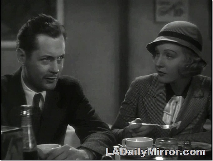 Man and woman sitting at lunch counter. She's holding a fork and looking at him. His hair is mussed and he looks a bit disheveled. 
