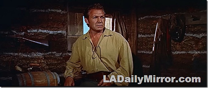 Man in interior of log constuction. He's wearing a frontier-style shirt. There is a crude window in the structure. Also a rifle. Man in interior of log constuction. He's wearing a frontier-style shirt. There is a crude window in the structure. Also a rifle.