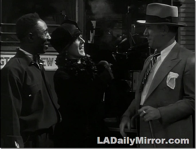 Exterior. Day. Two men and a woman are standing in front of a bus.  One man is in a bus employee's uniform. The other man is wearing a hat, coat and tie with a handkerchief in the pocket. He's smoking a cigarette. The woman is fashionably dressed with a hat. 