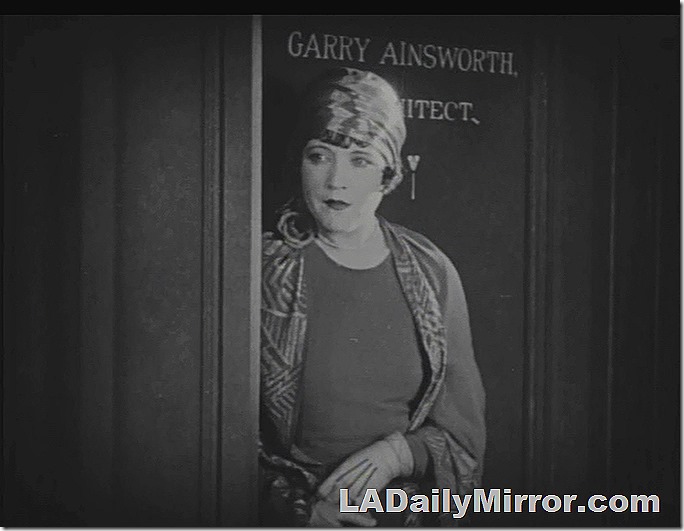 Woman in hat, coat and gloves stands in a doorway. 