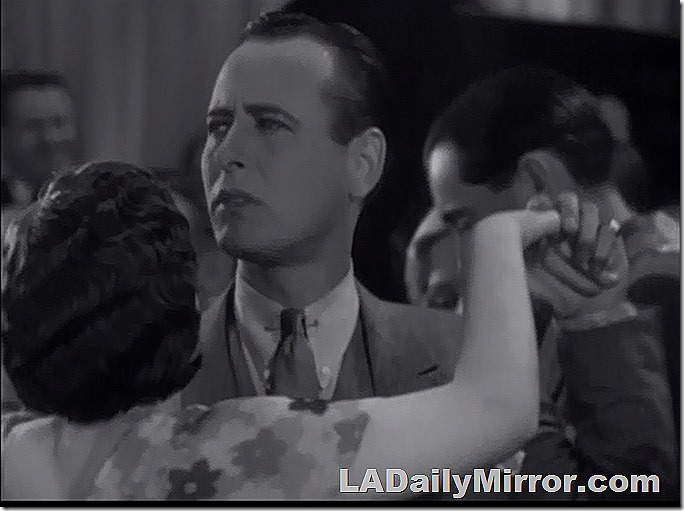 Man with neatly combed hair, coat and vest, tie with collar pin. Is dancing with a woman (face unseen). He looks concerned. 
