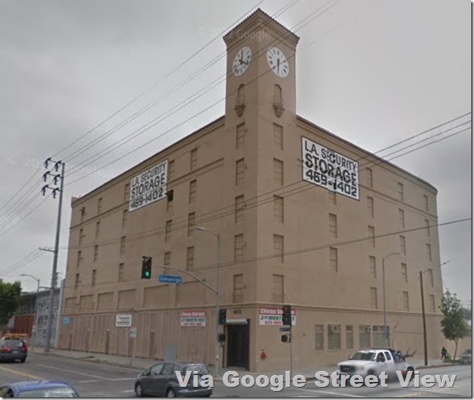 Gray sky. Beige building with clock tower. All windows painted over. 