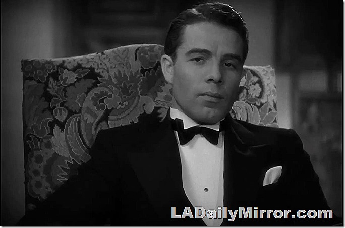 Man sitting in chair. He is wearing a tuxedo. 