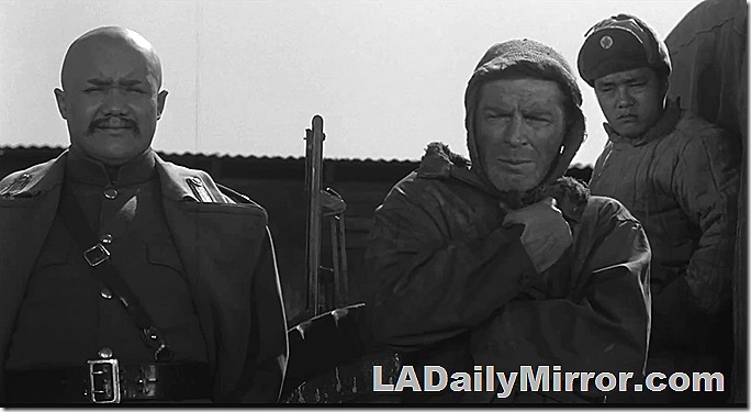 Asian colonel, left, in uniform. Man in center is bundled against the cold. At right, a soldier observes the scene