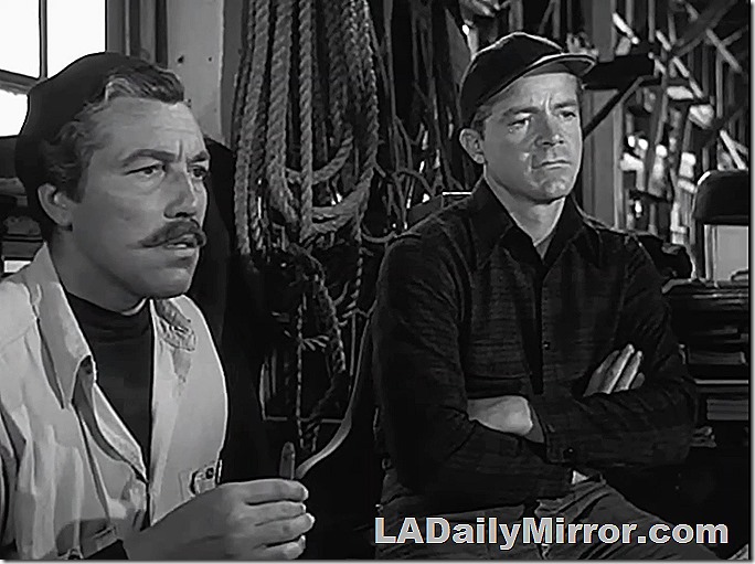 Men dressed for outdoor work. One has a mustache, a shirt over a sweatshirt. The other is wearing a cap and a flannel shirt