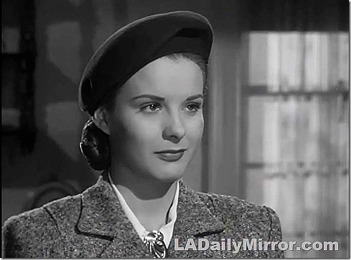 Woman in beret and coat. A broach is at the neck of her blouse. 