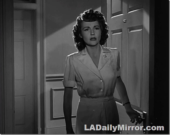 Woman in nurse's uniform, backlit in doorway. Looks into room, puzzled by whatever is going on. 