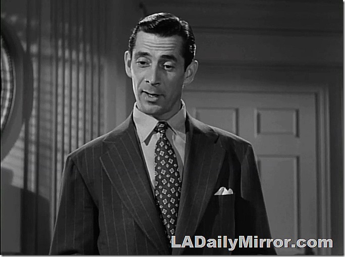 Man with dark hair. Wears pinstripe suit with wide lapels. Very busy tie. 