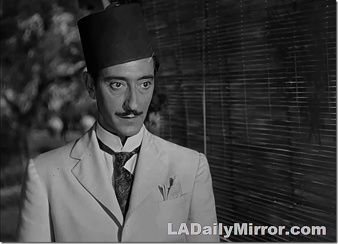 Man with a slight mustache wears white suit and fez, high collar with tie. 
