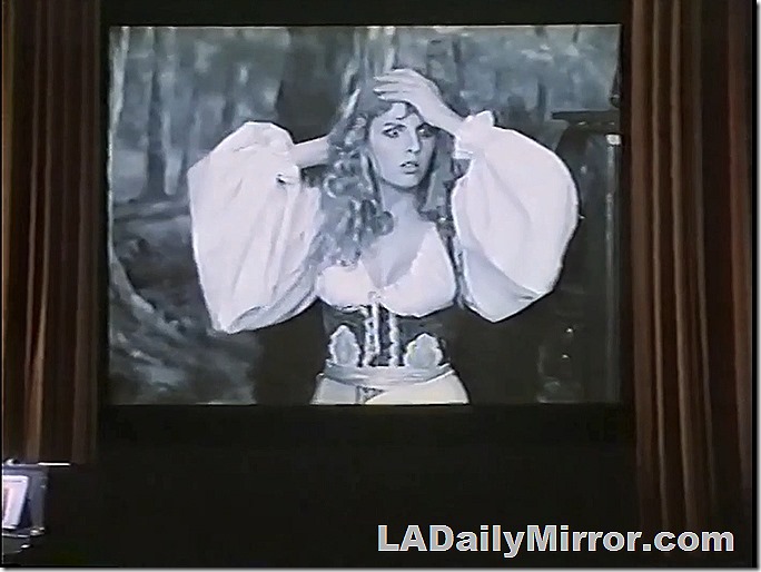 Woman on a movie screen in a pirate/gypsy outfit. Or something. 