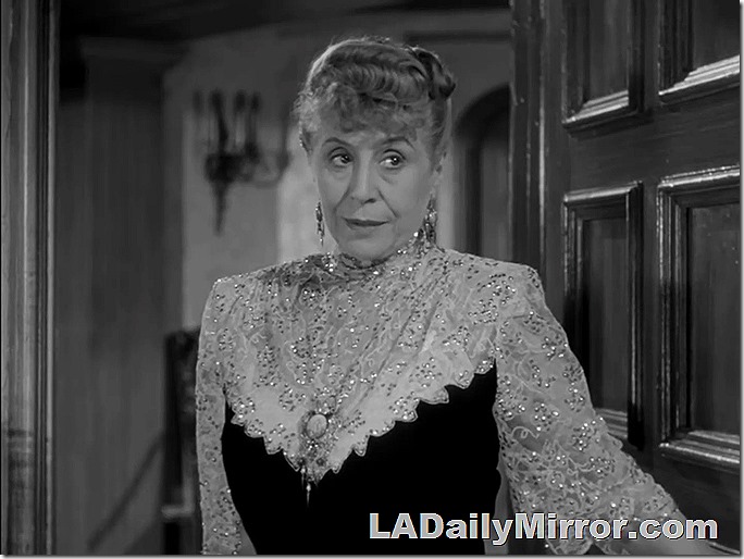 Woman in an elegant, but old-fashioned high-necked dress. Very sparkly with lots of jewelry.