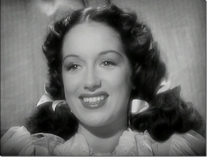 Woman smiling broadly. Her dark hair is tied back with two bows.  