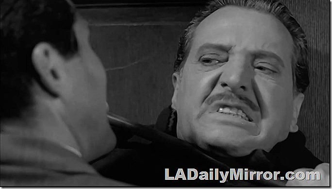 Man with mustache grimaces in an evil manner. 