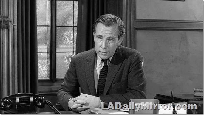 Man sitting at desk, he's wearing a suit coat and tie. 