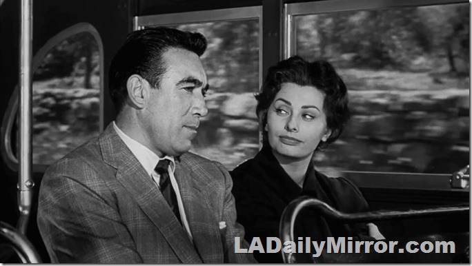 Mysterious couple riding a bus. He's wearing a coat and tie. She's wearing a dress. 