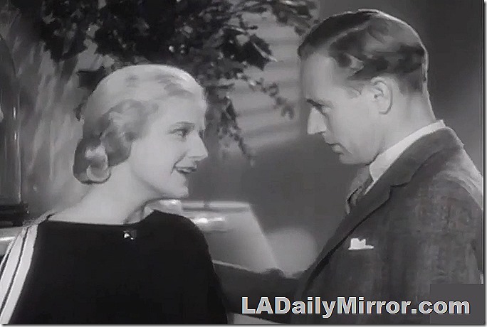 Blond woman in dark dress with stripes down the sleeves. Man in suitcoat and tie, with pocket scarf. 