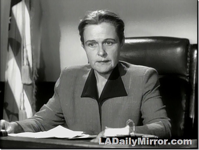 Mysterious woman in high-backed chair. A flag is in the background. 