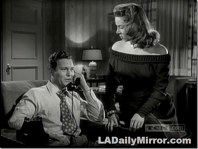 Man in shirtsleeves, tie pulled loose, talking on phone. A woman is nearby, listening. 