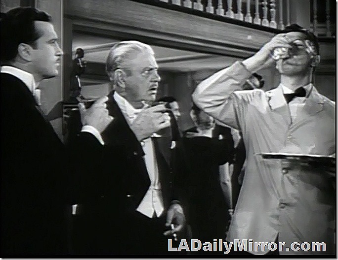 Men in tuxedos with martini glasses look disapprovingly at a mysterious companion. 