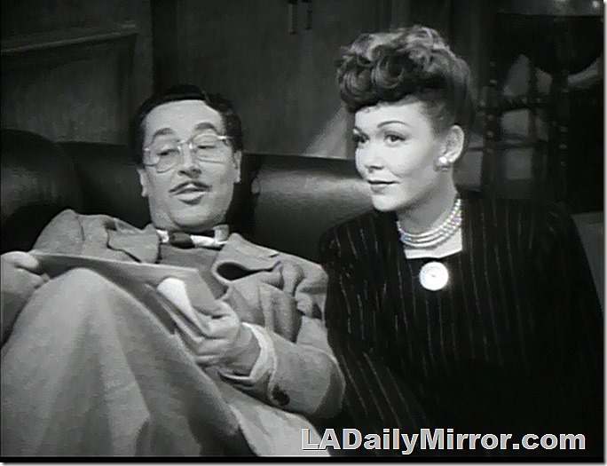 Man wearing glasses lying on a couch. Woman next to him is looking just off-camera. 
