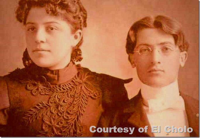 Latino couple. She is in a fine, embroidered dress, he wears a high collar and glasses. 
