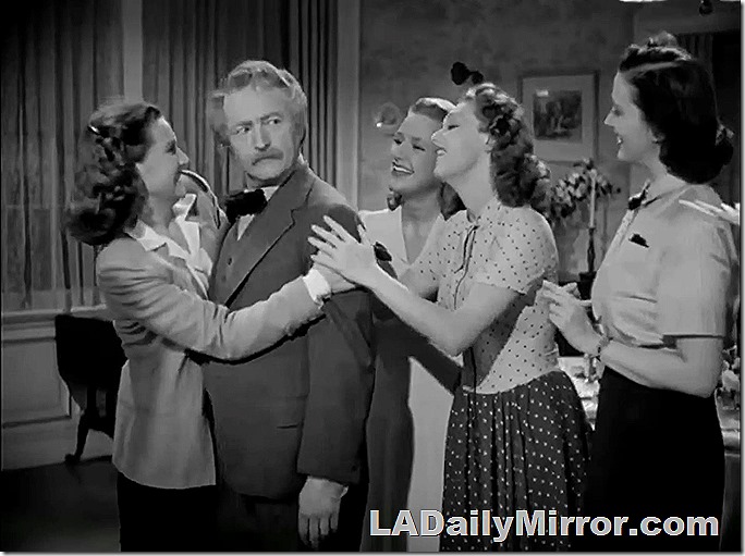 Distinguished man in bow tie with four younger woman. He is looking askance at them. 