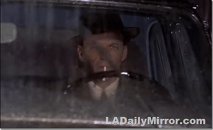 Man driving a car as seen through the windshield. he is wearing a hat and about to light a cigarette. 
