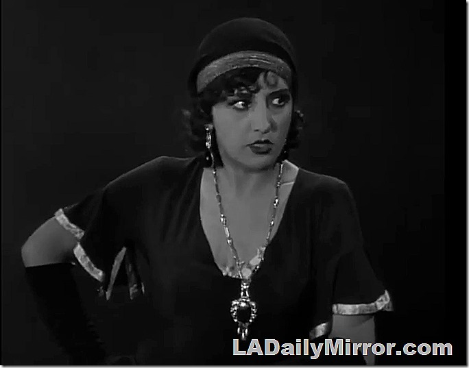 Woman with headband and long necklace with large pendant. 