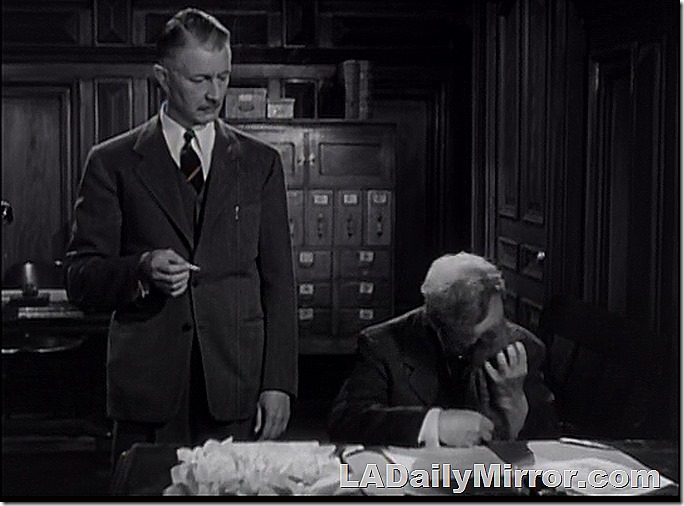 Neatly dressed mystery fellow smokes a cigarette while his rumpled companion hides his face. 