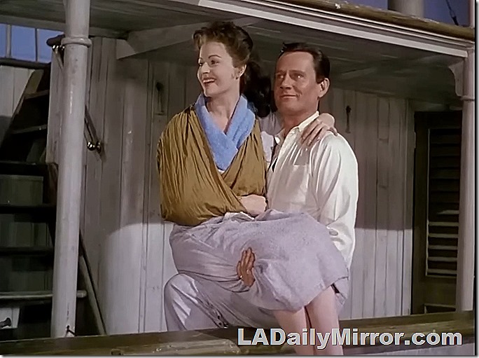 Mystery man holds mystery woman, who has her arm in a sling. 