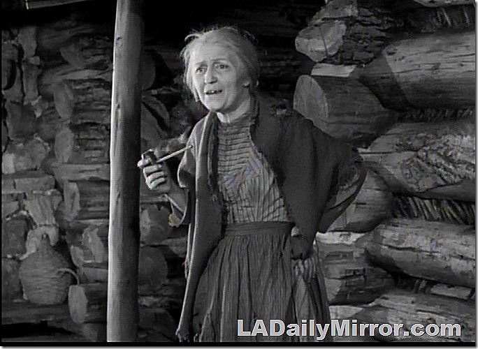 Pioneer woman with pipe outside log cabin