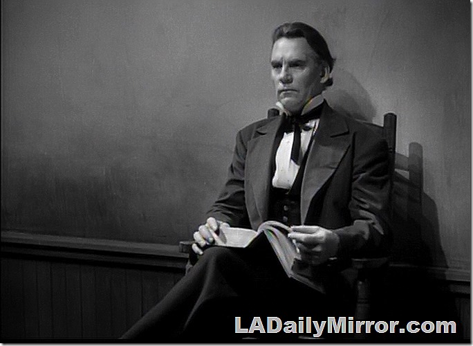 Man in coat and high collar sitting in chair