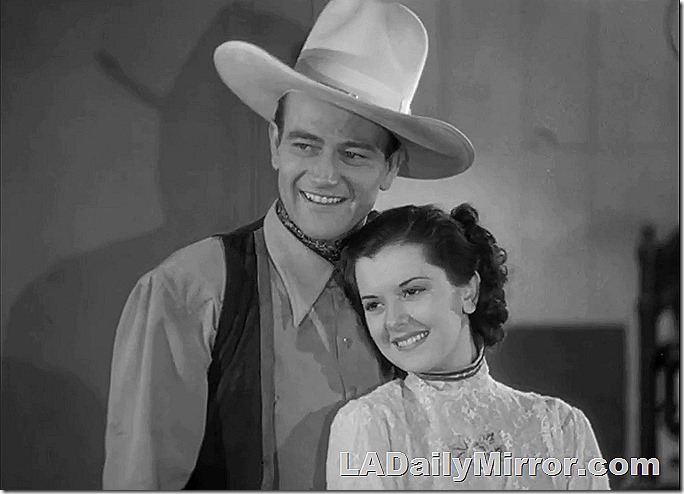 Tall man in cowboy hat and vest with lovely lady not wearing cowboy hat. 